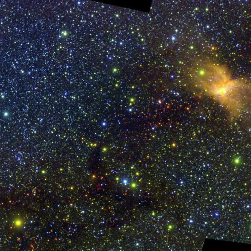 An infrared view of a star-forming region, showing a glowing cloud of dust and gas surrounded by a dense field of stars.
